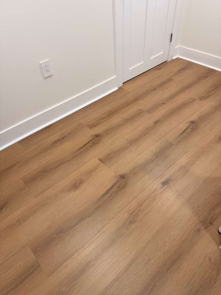Bedroom corner showing the plank meeting new white baseboard, with the closet threshold squared off.