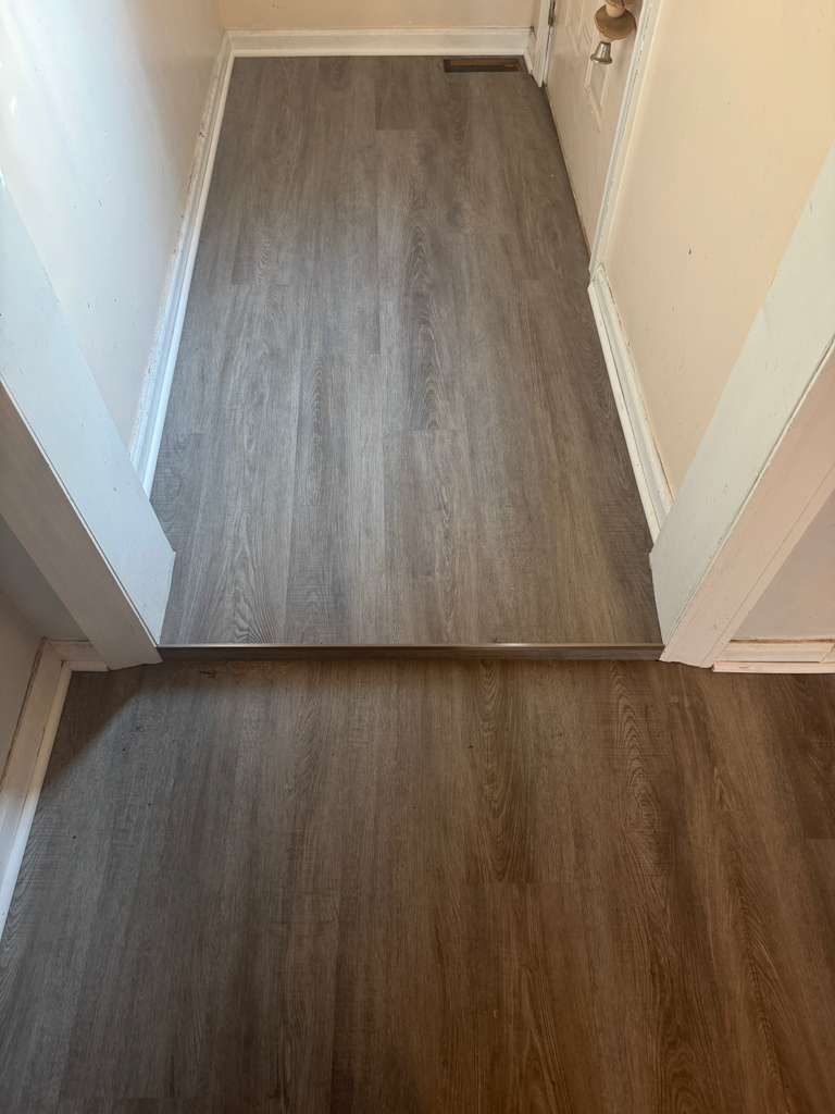 Two different plank colours meeting at a doorway with a metal transition strip set flush between them.